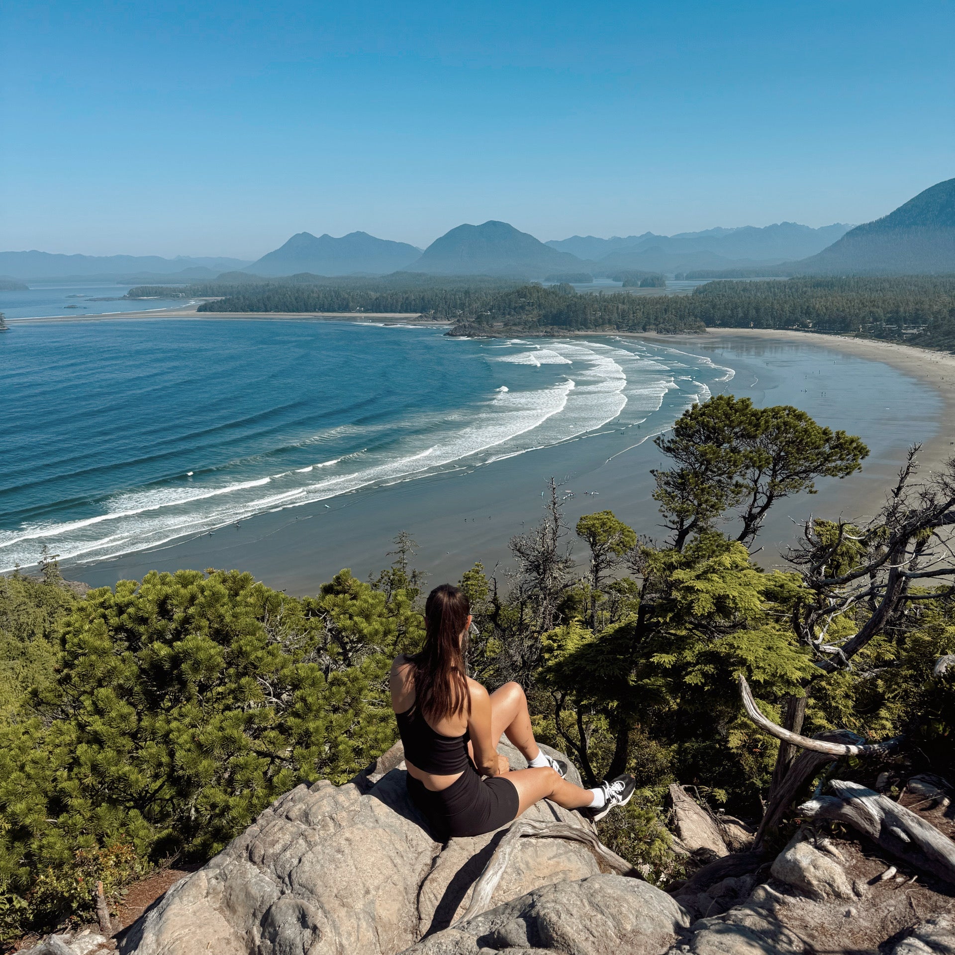 Person sitting on a rock overlooking a scenic coastal view with mountains and ocean.